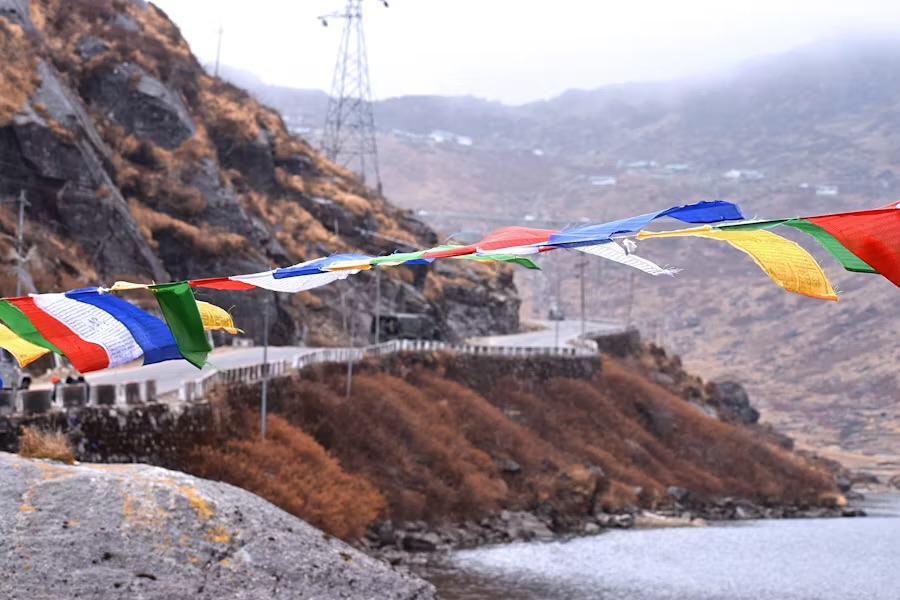 Buddhist prayer flags strung above a mountain road beside a lake on the high ground east of Gangtok