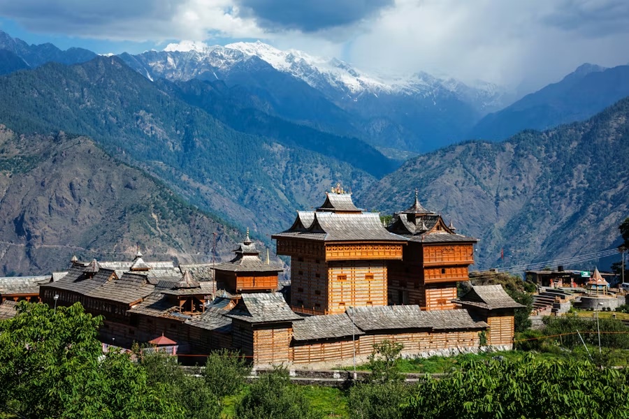 A traditional timber Himalayan temple complex below a ridge of snow-covered peaks
