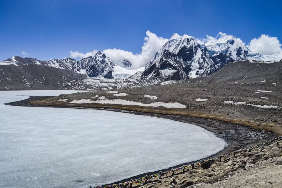 A frozen high-altitude lake below snow peaks in North Sikkim, prayer flags along the shore